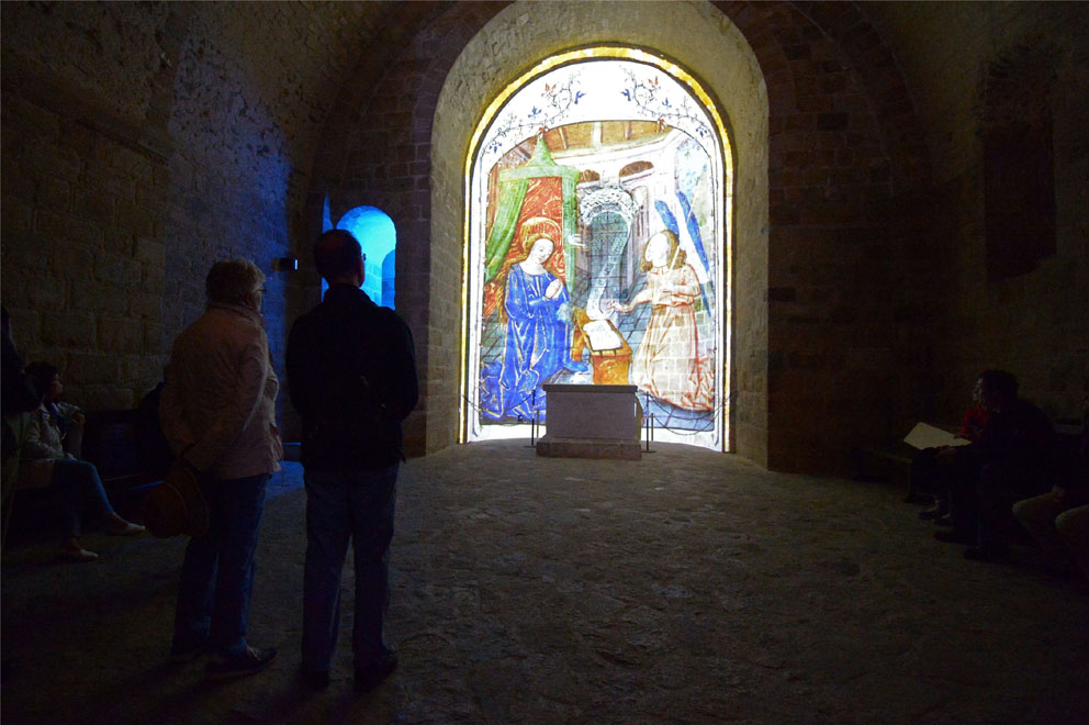 Deux personnes debouts de dos regardent l'alcôve de la chapelle St Martin où est projeté l'animation d'une enluminure.